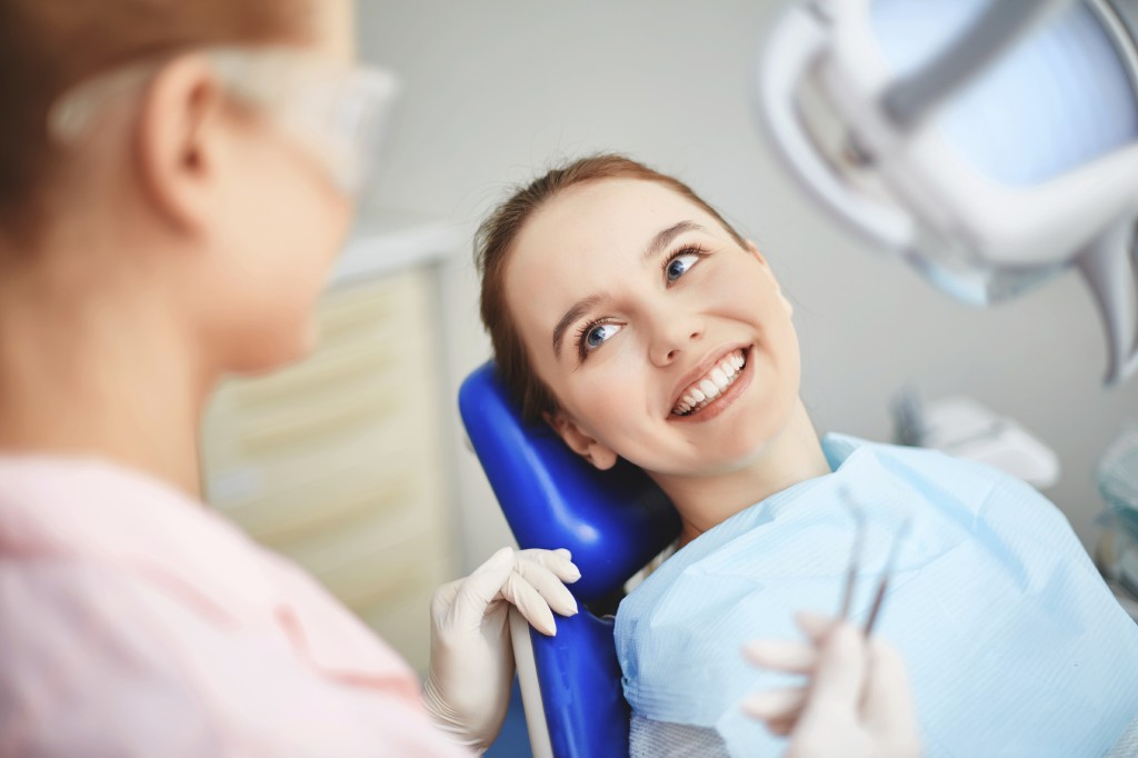 Young female sitting in dentist office and looking at her doctor with smile