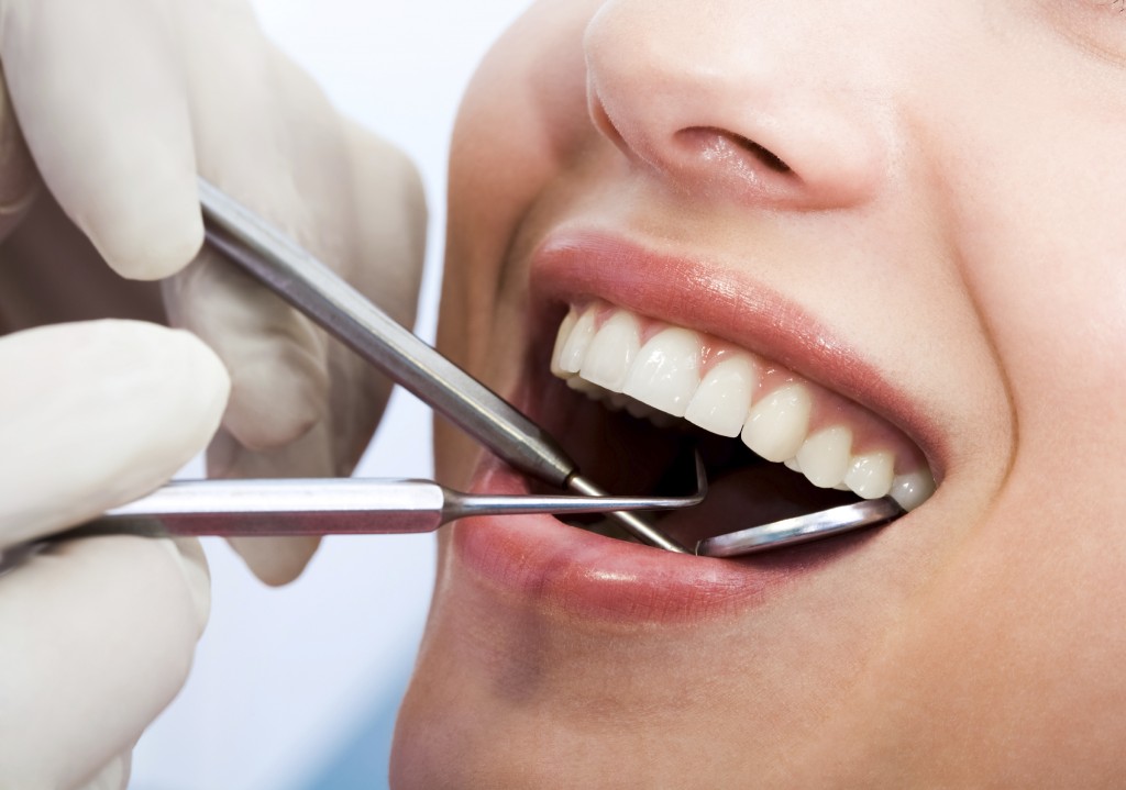 Close-up of patients open mouth during oral inspection with mirror and hook