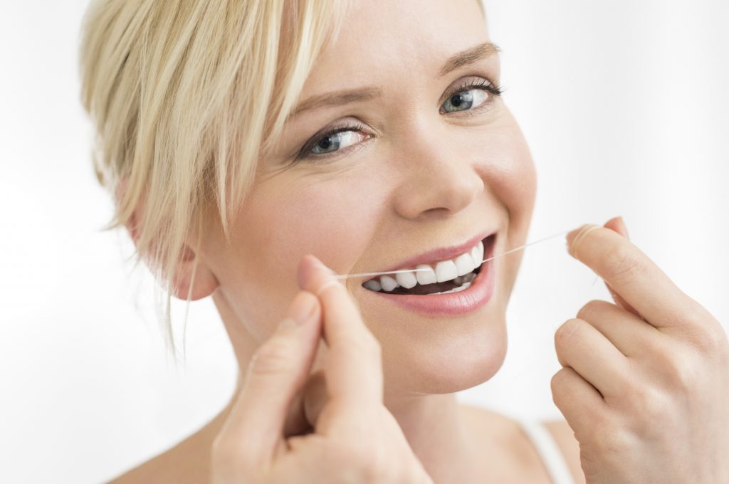 Portrait of young woman flosses her teeth with dental floss looking at camera