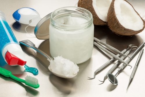 Selection of dentists tools on a stainless steel background with coconut oil, toothpaste, toothbrush and floss. Heaped dessert with coconut oil by jar.