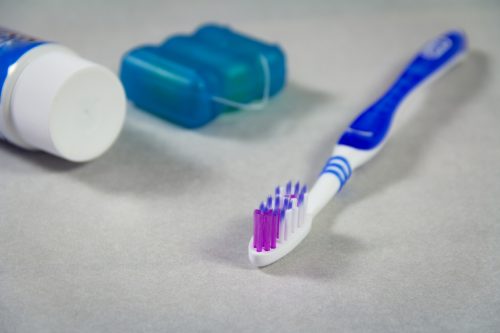 a toothbrush, toothpaste and dental floss on a grey surface
