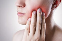 a man touching his cheek, indicating that he has a tooth problem