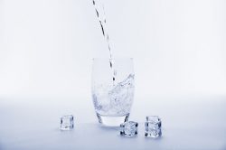 a glass with water getting poured into it, and ice cubes surrounding the glass