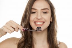 a woman smiling and holding a toothbrush with activated charcoal toothpaste on it