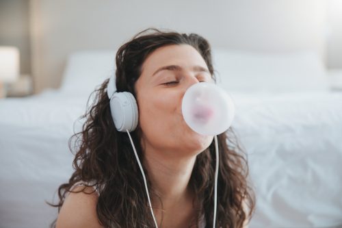 young woman making a bubble from a chewing gum and listening music with headphones