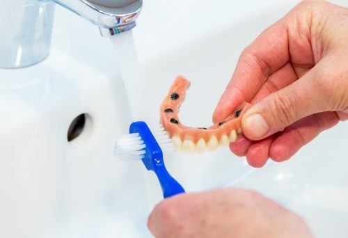 A man brushing dentures using a brush and water