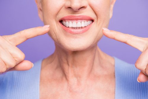 An older woman pointing at her perfect teeth and smiling